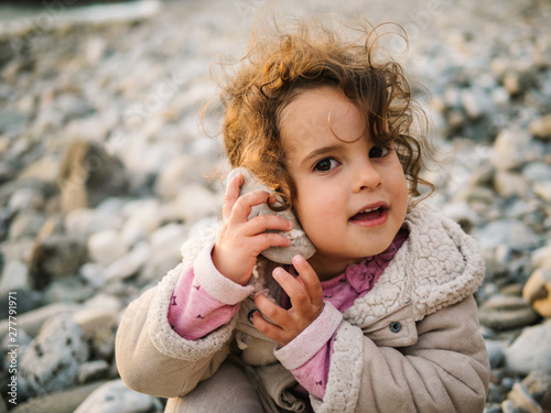 Portrait of little girl listening to conch with rapt on stony beach photo