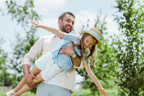 cheerful father holding in arms happy daughter in straw hat