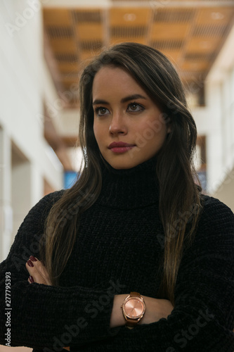 Pretty woman sitting along bookshelves and looking away