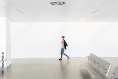 Motion blur of woman walking at contemporary white empty hallway.