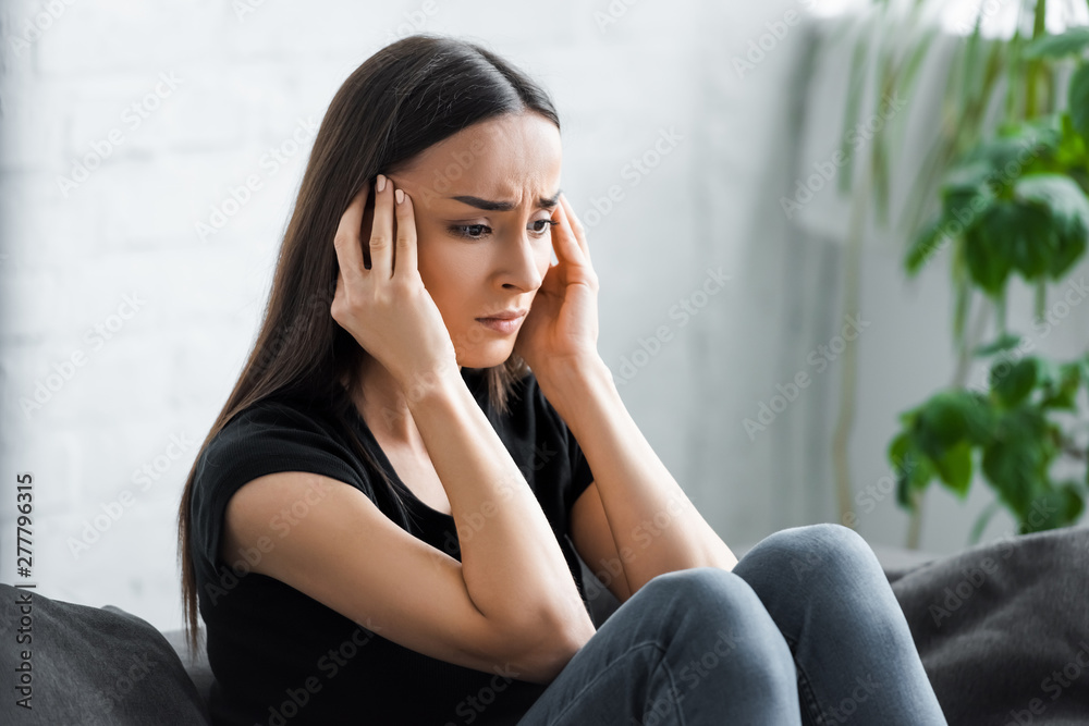 depressed young woman holding hands near head while sitting on sofa at home depressed young woman holding hands near head while sitting on sofa at home