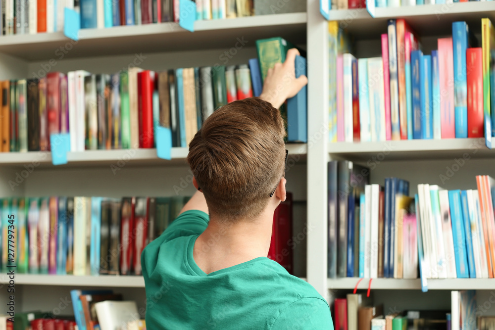 Young man taking book from shelving unit in library Young man taking book from shelving unit in library