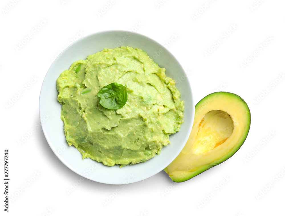 Bowl of tasty guacamole with basil and cut avocado on white background, top view