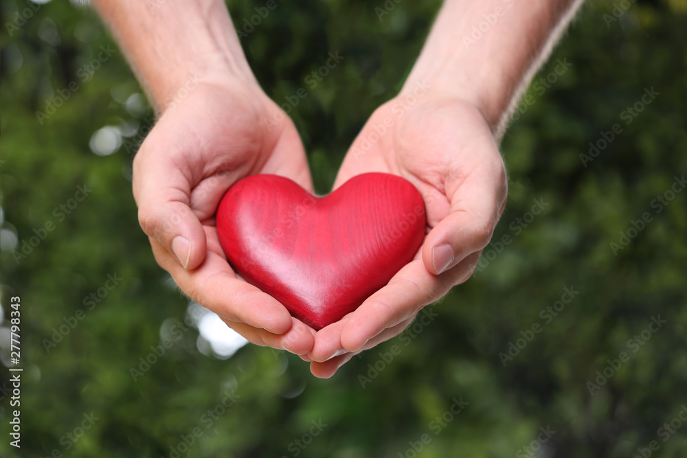 Young man holding red heart on blurred green background, closeup. Donation concept Young man holding red heart on blurred green background, closeup. Donation concept