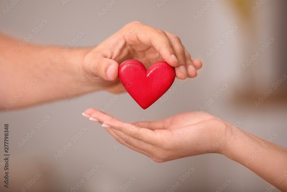 Man giving red heart to woman on blurred background, closeup. Donation concept Man giving red heart to woman on blurred background, closeup. Donation concept