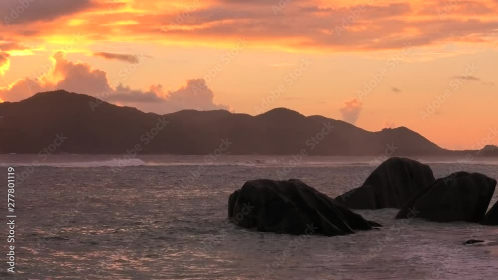 Colorful cloudy sky at twilight at scenic Anse Source d'Argent Beach in Seychelles, La Digue. Amazing landscape with shaped rock granite stone. Sun over the sea on the horizon.