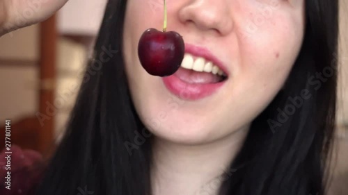 Young brunette woman eats red sweet cherry. Close-up.