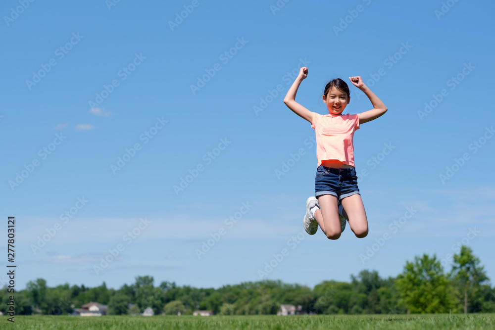 Happy young Asian girl jumping high in air, against background of summer blue sky.