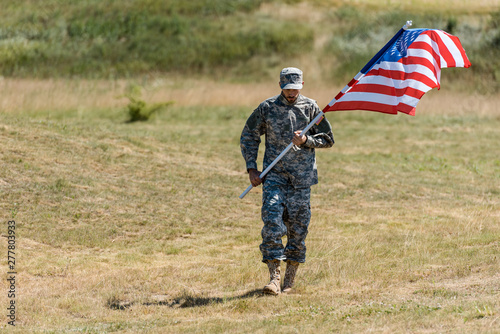selective focus of soldier walking and holding american flag in summertime