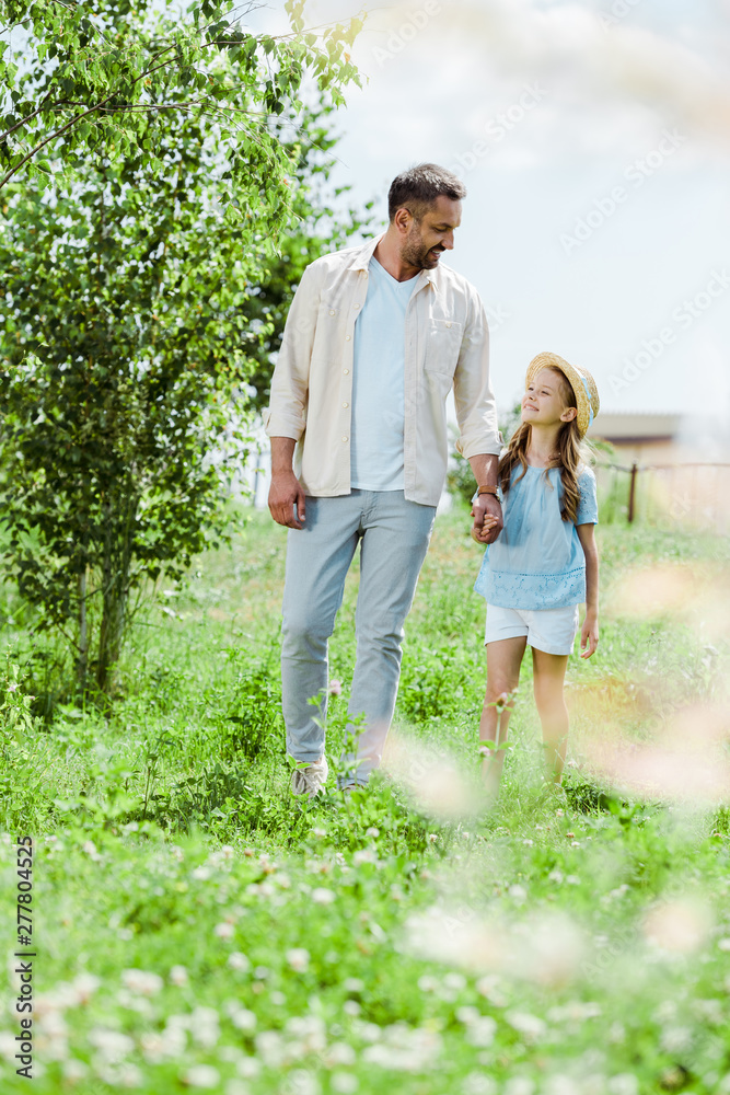 selective focus of father and daughter walking near green plants and holding hands selective focus of father and daughter walking near green plants and holding hands