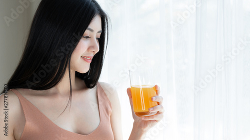 Beautiful beauty woman Asian cute girl feel happy drinking orange juice for good health in the morning , enjoying time in her home white bedroom background - lifestyle beauty woman concept