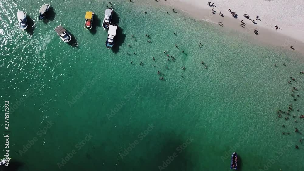 Drone view of people inside the blue ocean, and some boats in a tropical beach Pontal do Atalaia, Arraial do Cabo, Rio de janeiro