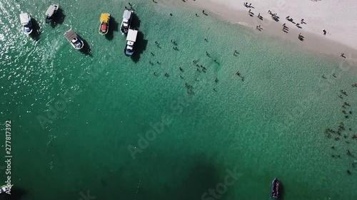 Drone view of people inside the blue ocean, and some boats in a tropical beach Pontal do Atalaia, Arraial do Cabo, Rio de janeiro