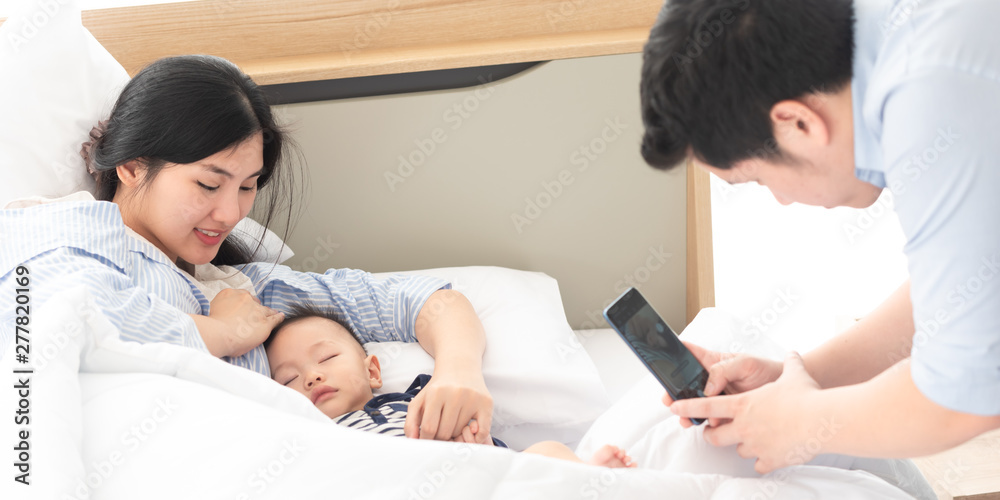 Obraz premium Father take photo of mother and their son while sleeping in bedroom