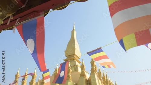 (Selective focus) Slow motion video of Laos flags waving in the foreground with the beautiful Pha That Luang in the background. Pha That Luang is a gold-covered large Buddhist stupa in Vientiane, Laos