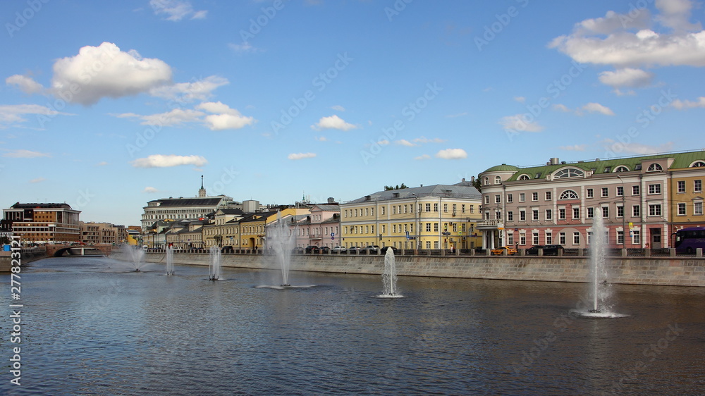 Russia, Beautiful colored old houses on Kadashevskaya embankment and fountains on the Vodootvodny canal in Moscow on a Sunny summer day on blue sky with white clouds background, wide cityscape