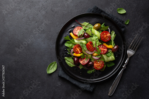 Fresh vegan salad with tomato, cucumber, bel pepper and olives salad on black plate
