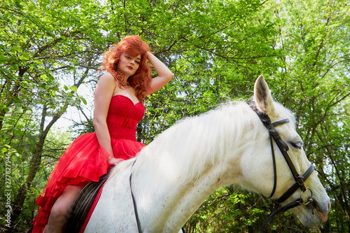 Girl in beautiful red dress on white horse in Park or forest. Photo shoot models and fashion