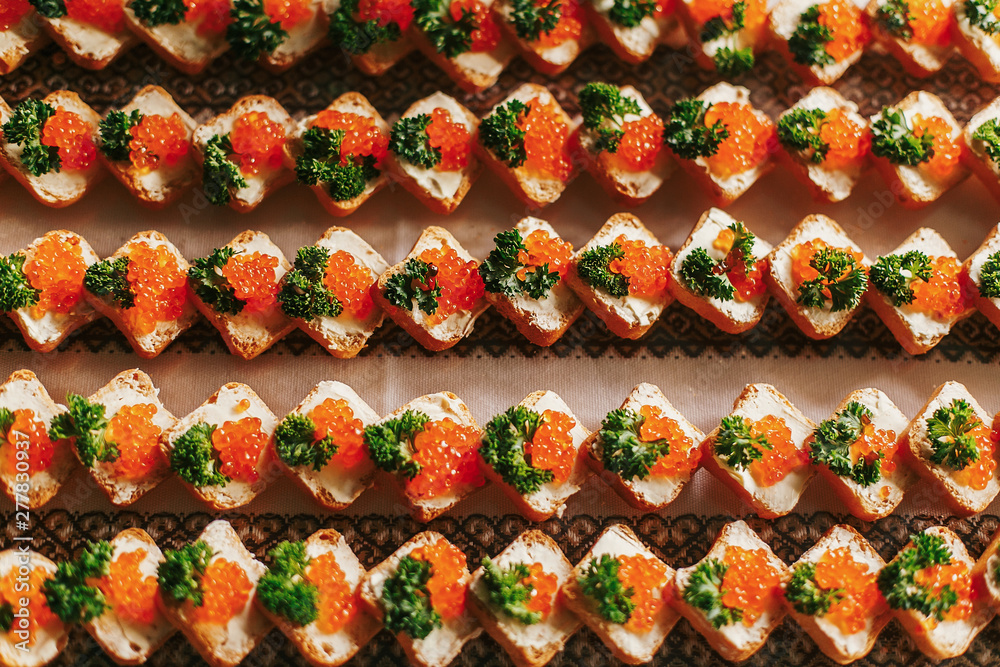 Delicious finger appetizers table at wedding reception. Caviar on bread canapes row top view on table at wedding or christmas feast. Luxury catering concept. Seafood flat lay