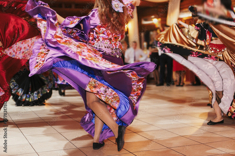 Beautiful gypsy girls dancing in traditional purple floral dress at wedding reception in restaurant. Woman performing romany dance and folk songs in national clothing. Roma gypsy festival