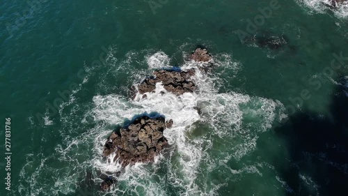 Drone flies over waves crashing against rocks in the ocean.