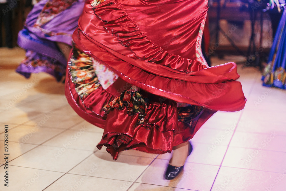 Beautiful gypsy girls dancing in traditional red floral dress at wedding reception in restaurant. Woman performing romany dance and folk songs in national clothing. Roma gypsy festival