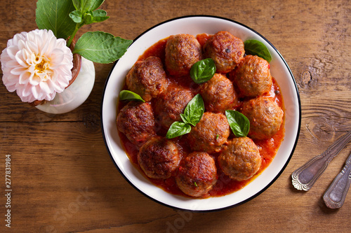 Meatballs in tomato sauce, garnished with basil in bowl on wooden table. View from above, top studio shot