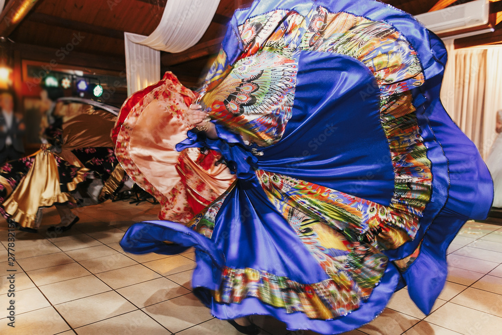 Beautiful gypsy girls dancing in traditional blue floral dress at wedding reception in restaurant. Woman performing romany dance and folk songs in national clothing. Roma gypsy festival