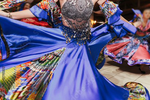 Beautiful gypsy girls dancing in traditional blue floral dress at wedding reception in restaurant. Woman performing romany dance and folk songs in national clothing. Roma gypsy festival