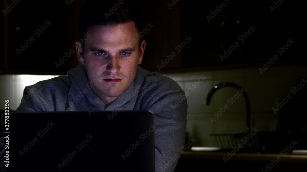 Cyber Criminal Using Laptop With Face Illuminated By Screen Cyber Criminal Using Laptop With Face Illuminated By Screen