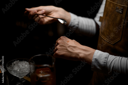 Male bartender holding a spoon and put a drop on the hand