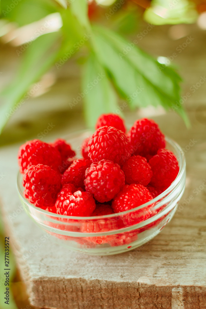 glass bowl full of raspberries on wooden garden table background glass bowl full of raspberries on wooden garden table background