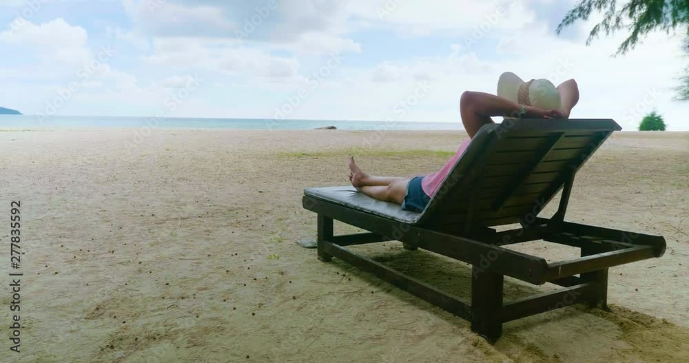 Summer beach vacation concept, Happy young Asian woman with hat relaxing on beach chair and put hand behind her head. Summer beach vacation concept, Happy young Asian woman with hat relaxing on beach chair and put hand behind her head.