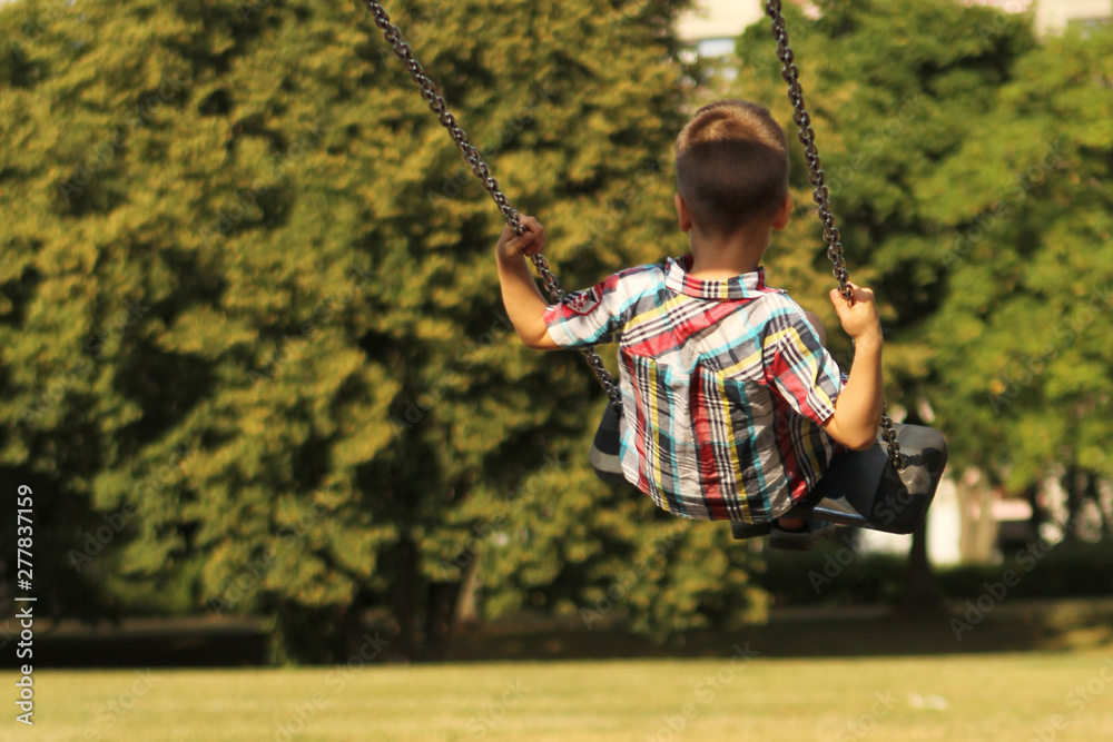 boy in a plaid shirt swinging on a swing in the park