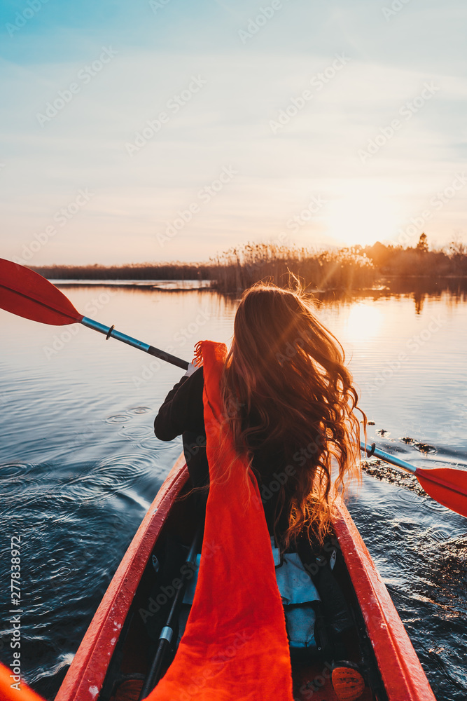 Back view of happy cute girl holding paddle in a kayak on the river - obrazy, fototapety, plakaty 