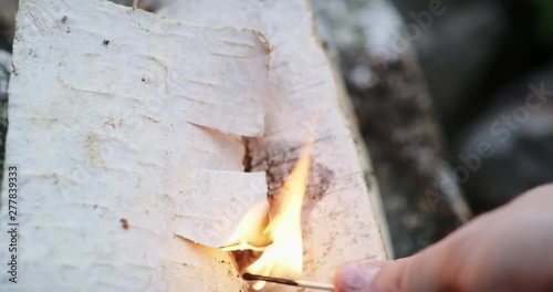 Close-up of a hand lights up a campfire with sticks.