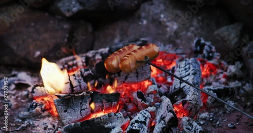 Grilling sausages over a campfire, roasting sausages.