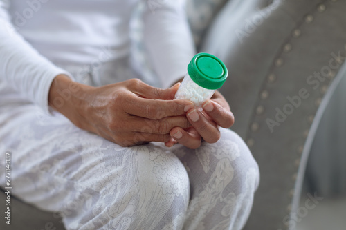 Woman sitting on a couch while holding a small pill bottle