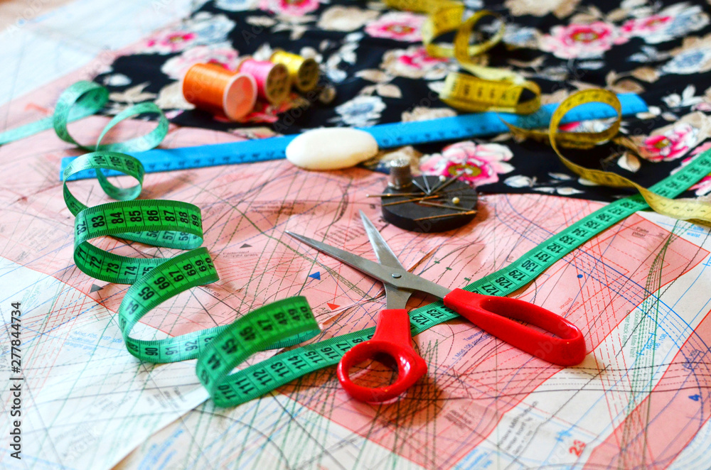 Essentials of the measuring and cutting textile or fine cloth. Work table of a tailor: Ruler, pattern, scissors, thread, needle, cloth, drawing tool, thimble. Tailoring industry dressmaking tools