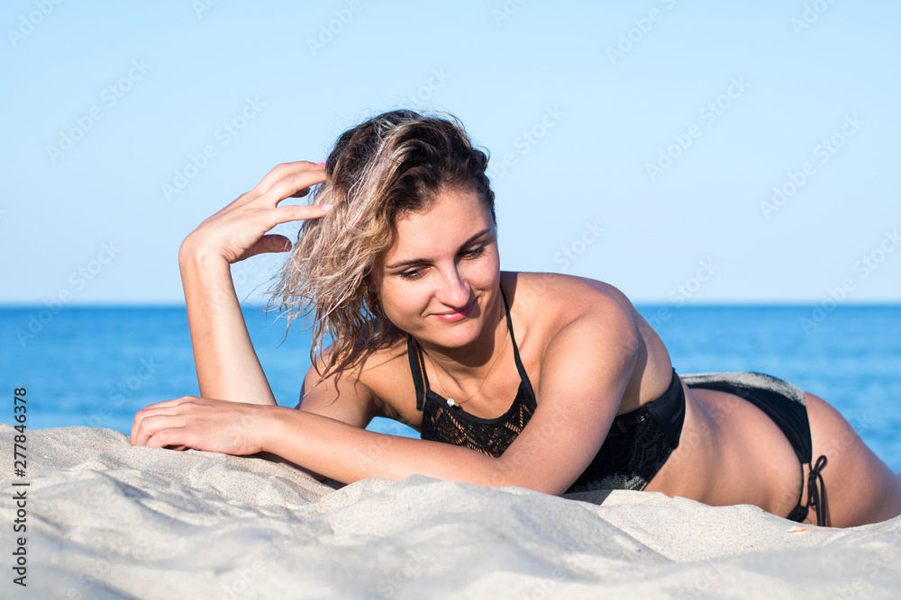 tanned young attractive woman with curly hair in black swimsuit on the beach, lying on the sand tanned young attractive woman with curly hair in black swimsuit on the beach, lying on the sand