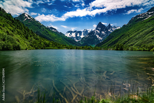 Fototapeta Naklejka Na Ścianę i Meble -  Landscape, mountain lake with clear water in the foreground, against the top of the mountains with a glacier and a blue sky with clouds.