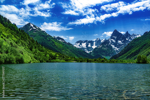 Landscape, mountain lake with clear water in the foreground, against the top of the mountains with a glacier and a blue sky with clouds. photo