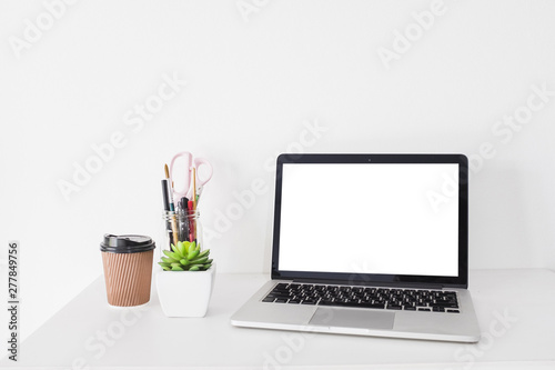 Laptop with blank white screen and disposal cup on desk
