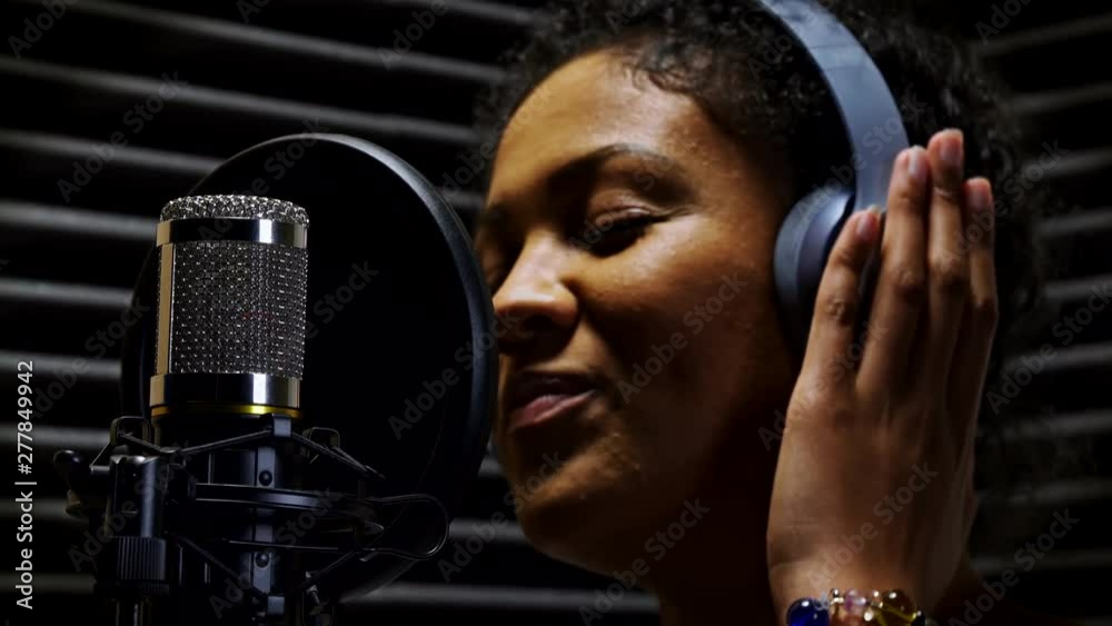 Female Vocalist Wearing Headphones Singing Into Microphone In Recording Studio
