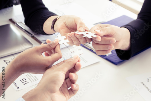 Closeup of businesspeople holding jigsaw puzzle.