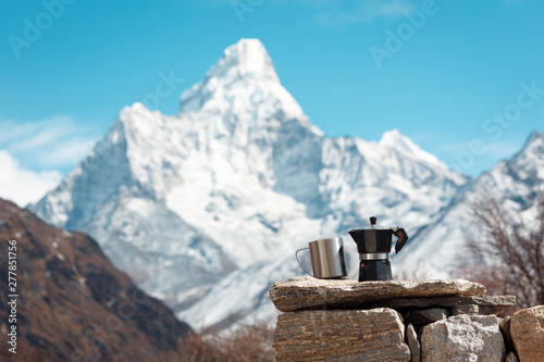 Mug and coffee maker stand on the stones. Mount Ama Dablam is blurred. Everest trekking Nepal.