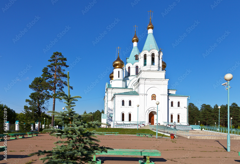 Beautiful Holy Trinity Cathedral on a sunny summer day against the blue sky in the Siberian city of Angarsk, Irkutsk region. Church cozy courtyard with green lawns and coniferous trees. Cityscape