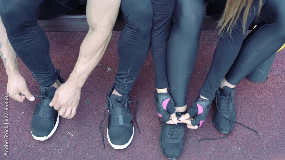 Close-up of hands of man and woman tying shoelaces on sneakers before training outdoors Close-up of hands of man and woman tying shoelaces on sneakers before training outdoors