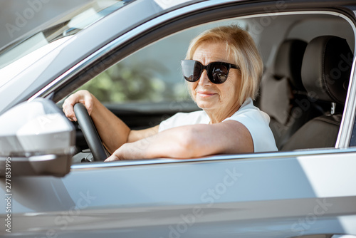 Portrait of a senior woman driver sitting in the modern car, looking out the window. Concept of an active people during retirement age © rh2010