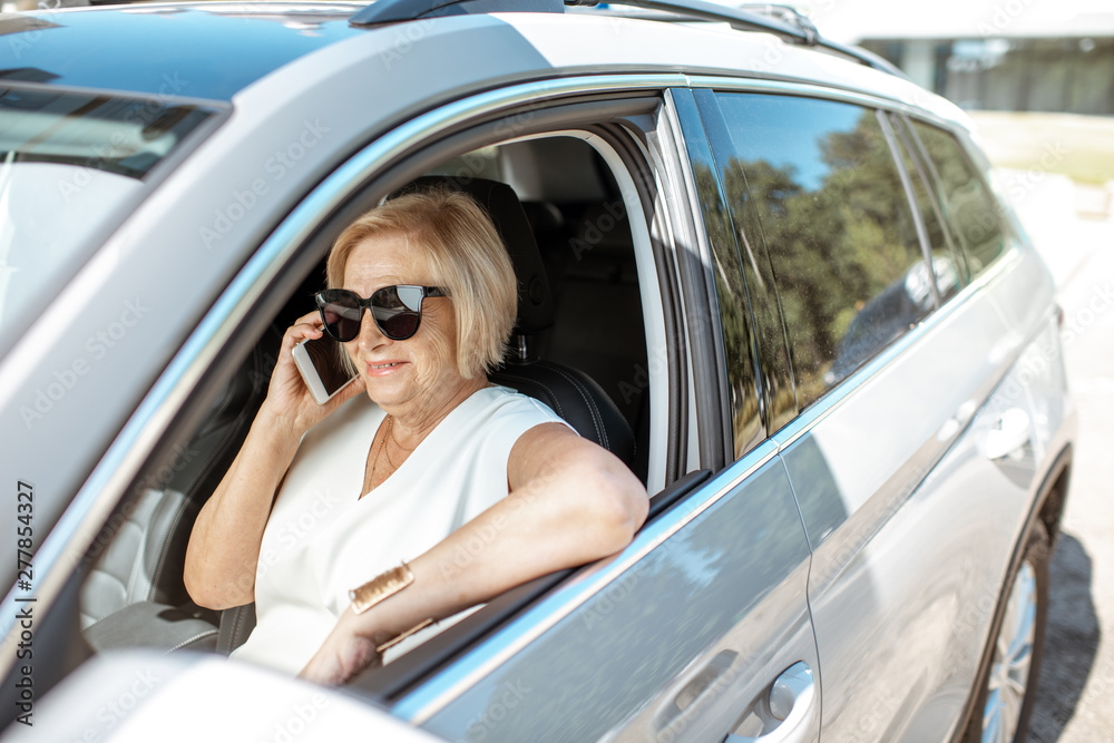 Beautiful senior business woman talking with phone while driving a modern car. Concept of an active people during retirement age